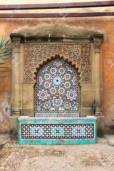 A traditional Moroccan zellige fountain set into a wall — the central element of the Andalusian garden tradition, with its geometric tilework and horseshoe arch surround representing the architectural language of Al-Andalus continued in Morocco