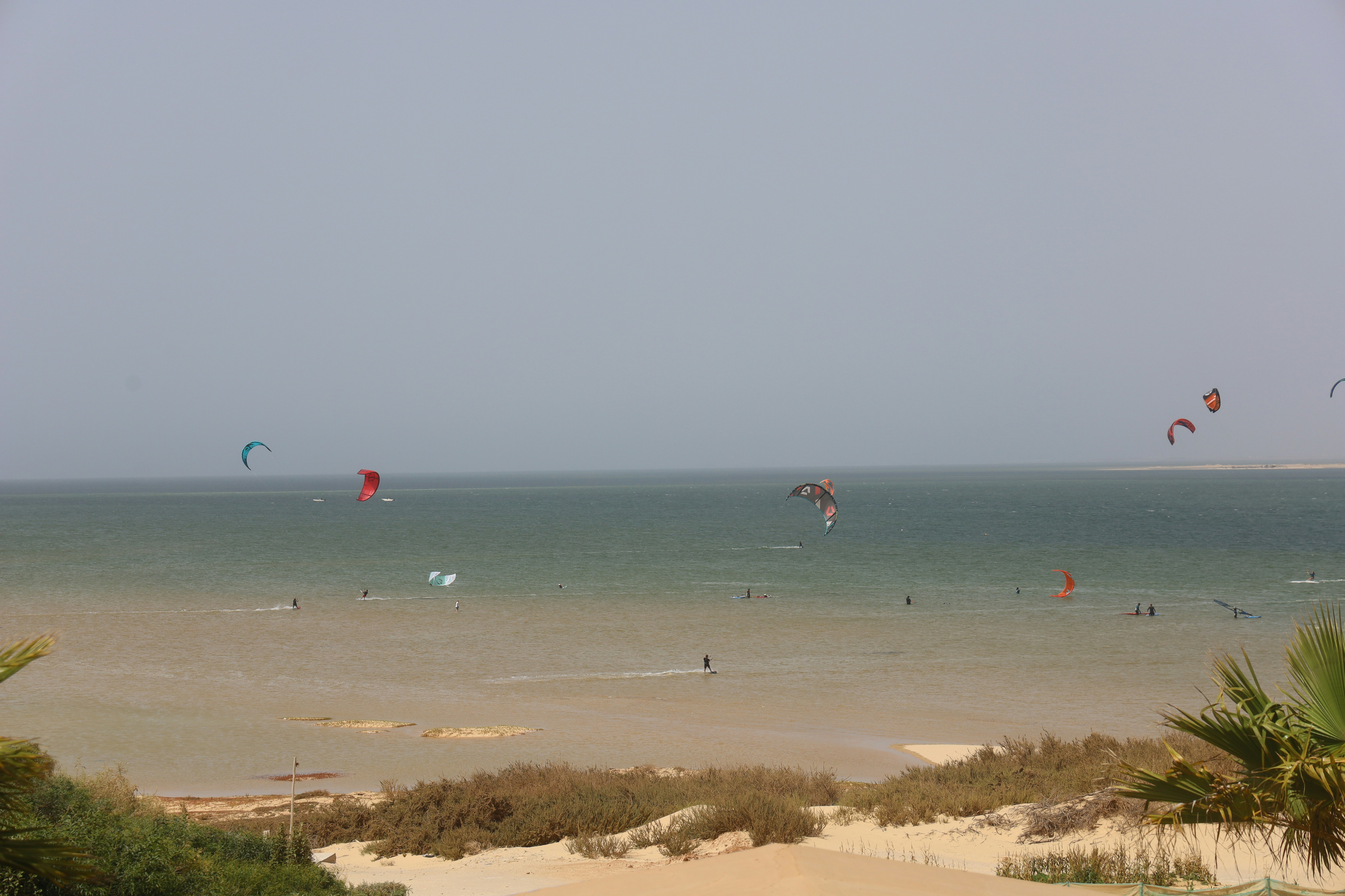 Kitesurfer flying across the flat turquoise water of the Dakhla lagoon with Saharan dunes in the background