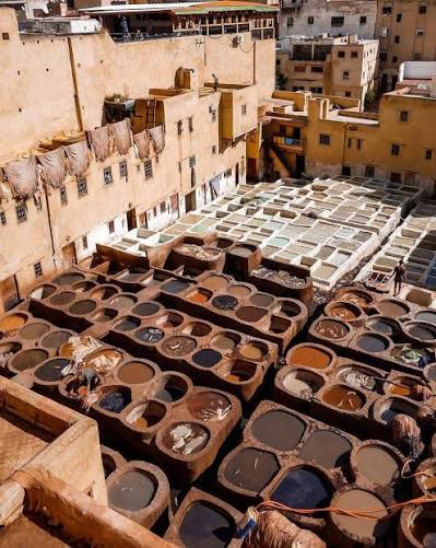 Chouara tanneries in Fes — coloured dye pits viewed from above with workers treading hides