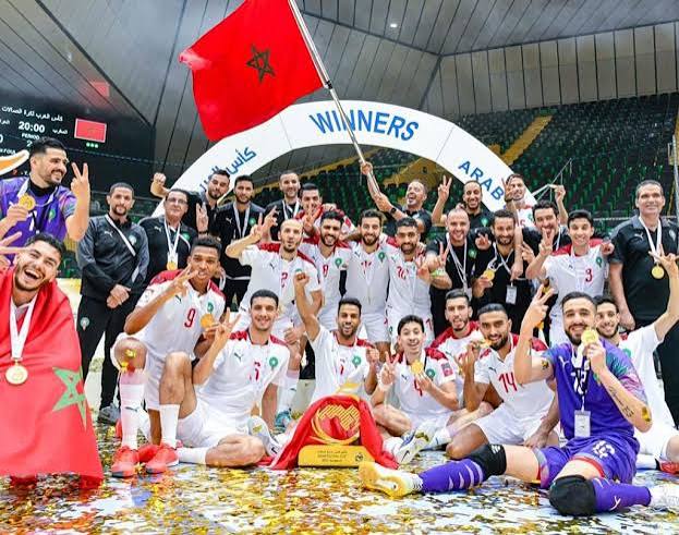 Morocco's men's futsal squad celebrate their record-equalling third Futsal AFCON title in Rabat, 2024, waving a Moroccan flag under a WINNERS arch