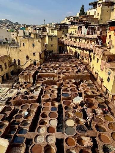 Rows of round stone vats filled with dyes and treatment liquids at the Chouara tannery in Fez, surrounded by medina buildings
