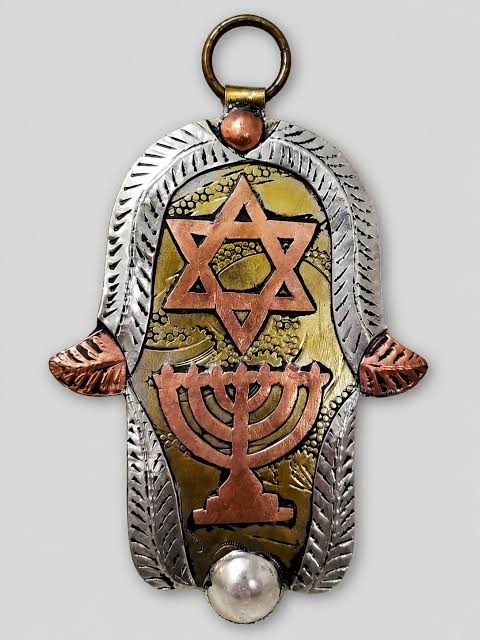 A metal hamsa-shaped pendant decorated with a Star of David and a menorah, with a pearl at its base