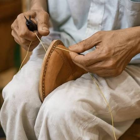 Close-up of hands stitching a tan leather piece with a needle and thread
