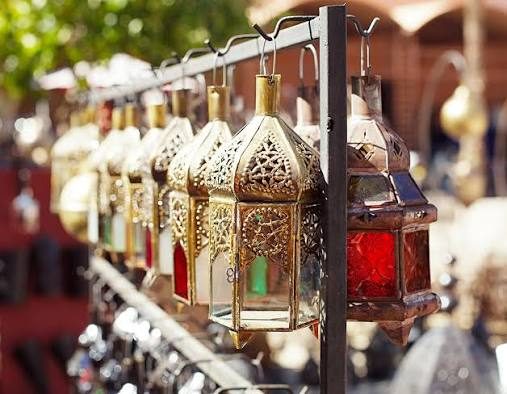 Metal lanterns with coloured glass panels and pierced tops hanging on a rail in a market