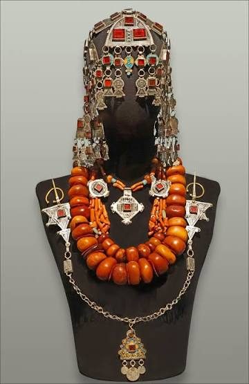 A ceremonial ensemble of silver headdress, pendants and necklaces with large amber-coloured beads displayed on a dark stand