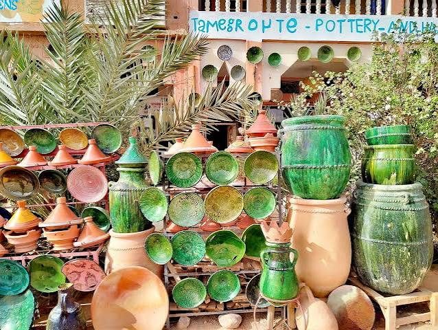 Green-glazed jars, bowls and vessels displayed outside a pottery whose sign reads Tamegroute Pottery