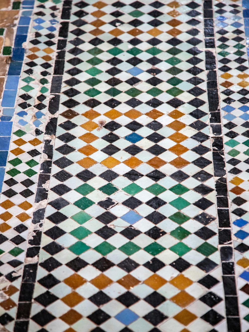 Small glazed zellige pieces in black, white, green, ochre and blue set in a diamond lattice between dark borders